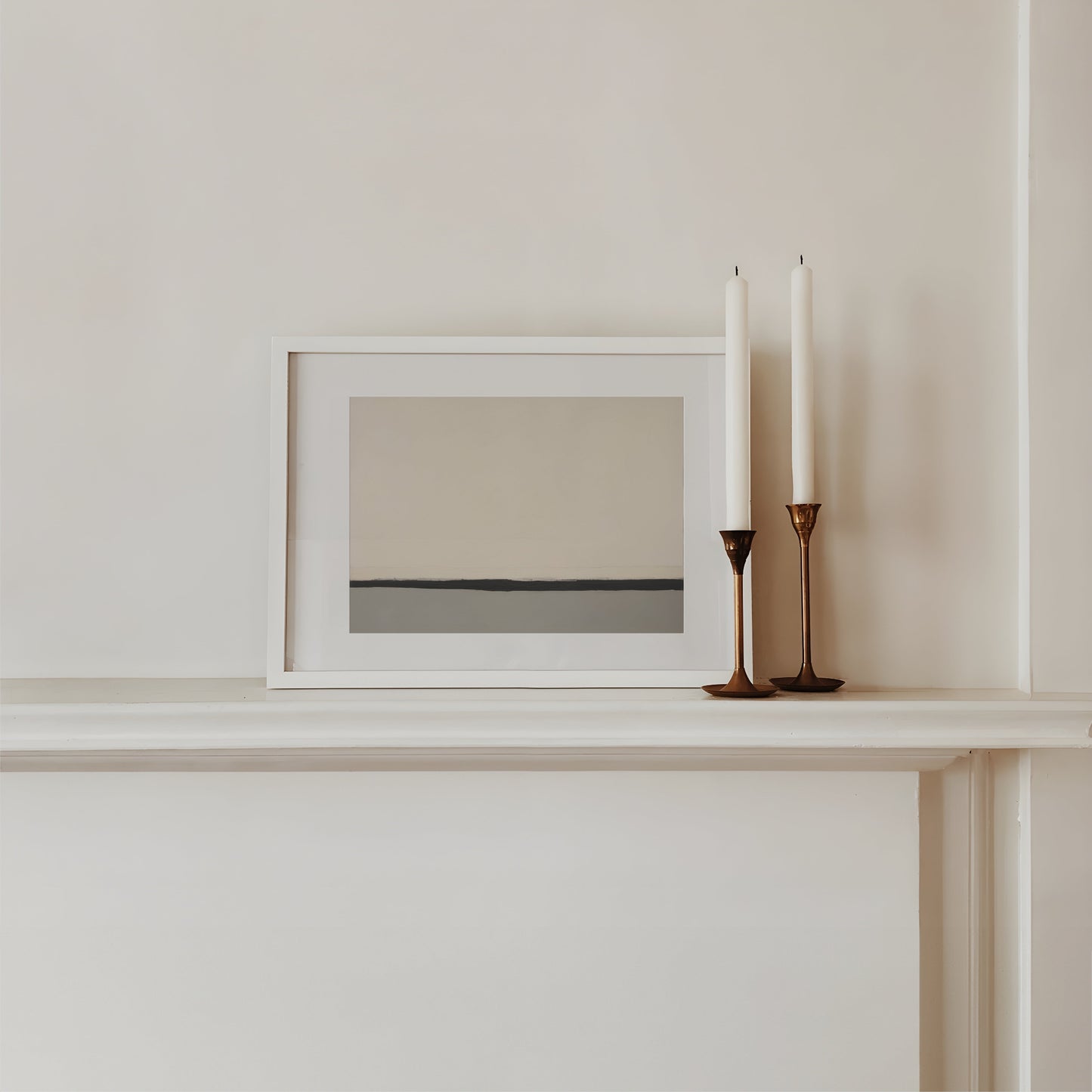 Framed artwork on a shelf with two candles in candlesticks.