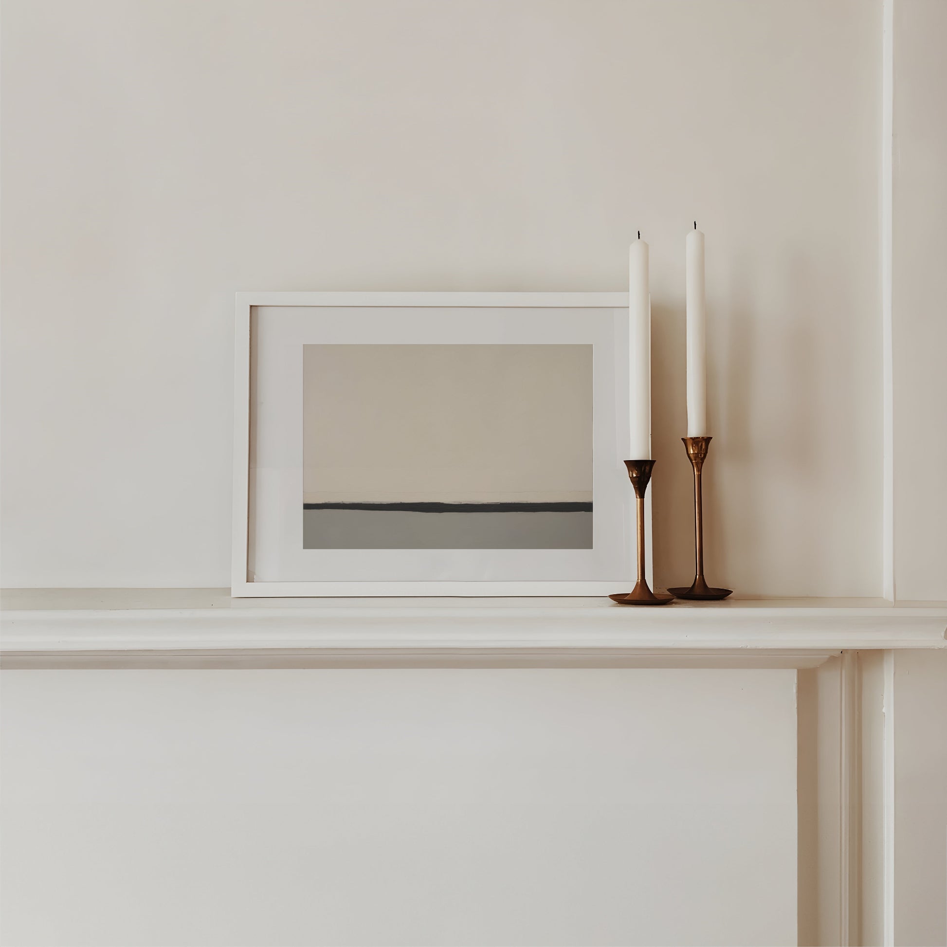 Framed artwork on a shelf with two candles in candlesticks.